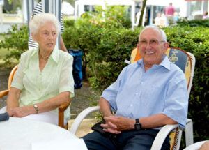 Sommerfest: Ältere Dame und älterer Herr sitzen gut gelaunt und bei Sonnenschein an einem Gartentisch